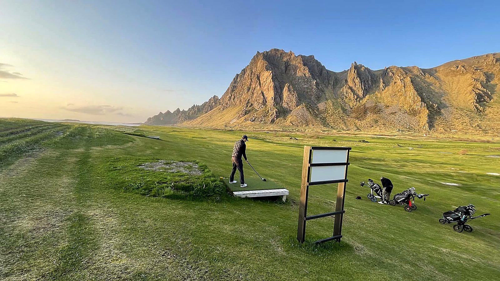 Golfer på utslag med fjell i bakgrunnen
